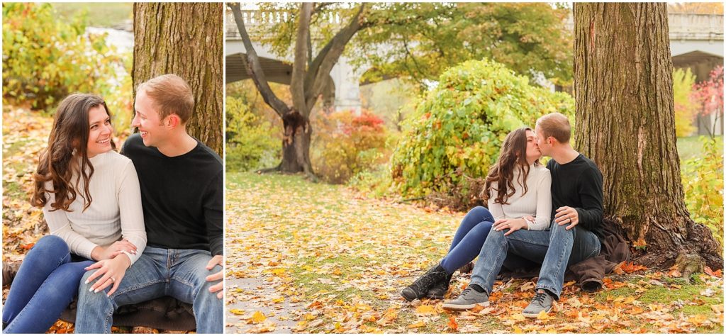 engaged couple sitting under tree with fall leaves