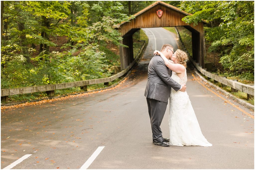 bride and groom kiss under covered bridge